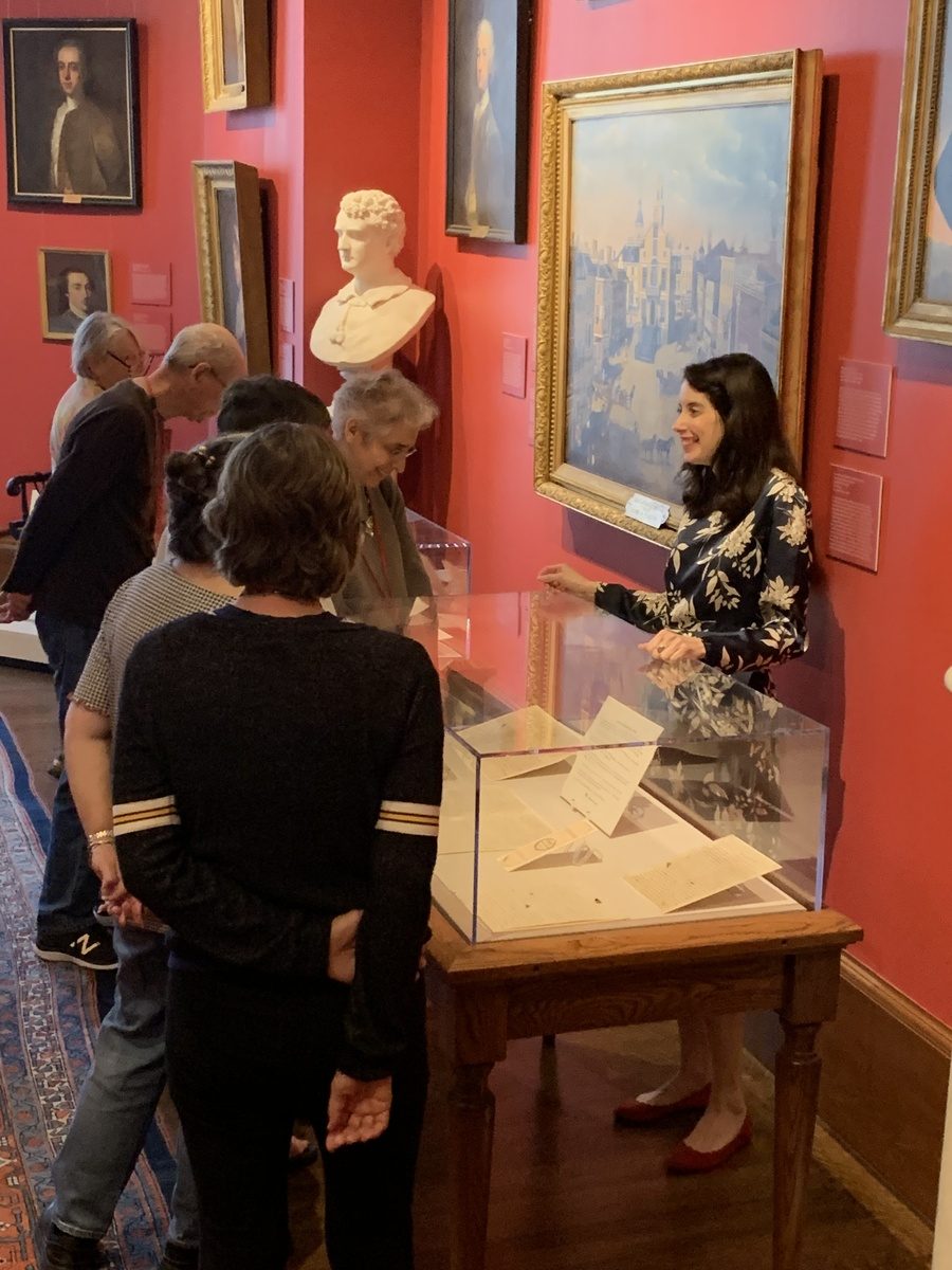 Woman standing behind exhibit case speaking to visitors